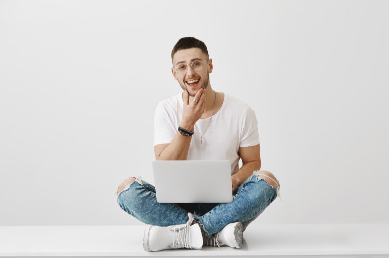 Score de crédito | Foto de um homem sorridente sentado no chão com um notebook no colo | Como limpar o seu nome 