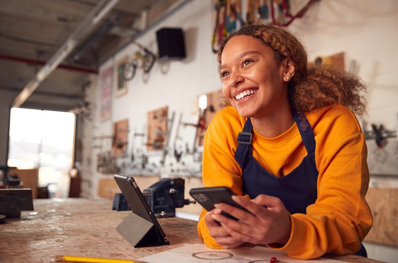 Trabalho autônomo | Foto de uma atendente sorrindo no balcão segurando um celular | Dúvidas sobre dívidas | Eu Dou Conta