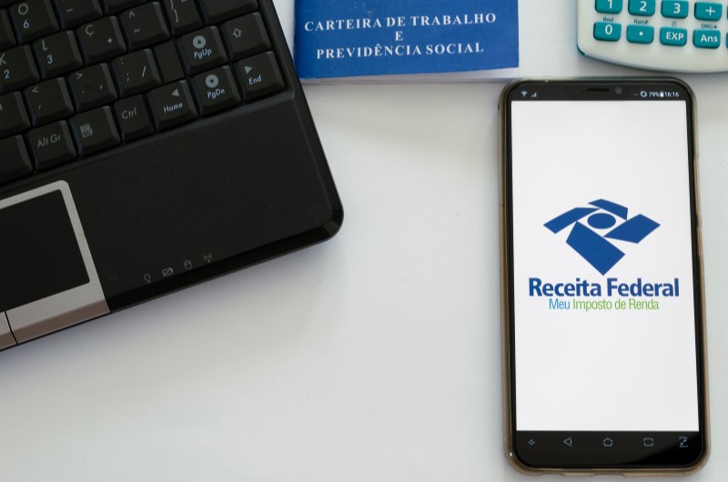 Como declarar imposto de renda autônomo | Foto de um celular com o programa da Receita Federal, notebook, carteira de trabalho e calculadora | Dúvidas sobre dívidas | Eu Dou Conta