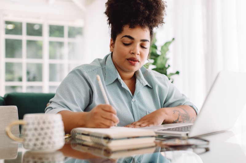 Faça um planejamento para as atividades de lazer | Mulher concentrada enquanto escreve em um caderno | Eu Dou Conta | Blog da Tenda 