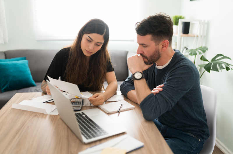 Casal analisando documentos financeiros com um laptop na mesa, representando o planejamento de custos relacionados ao ITBI na compra de um imóvel