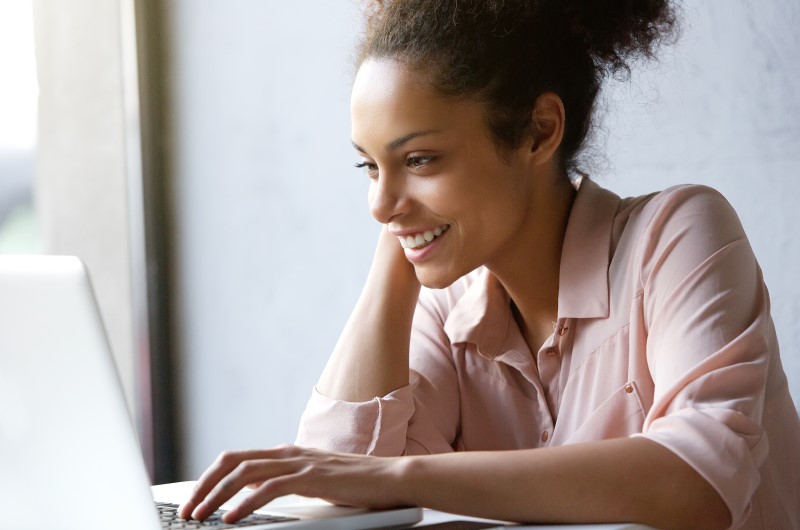 Mulher jovem sorridente olhando para o computador | Aprenda a evitar o nome sujo | Eu Dou Conta