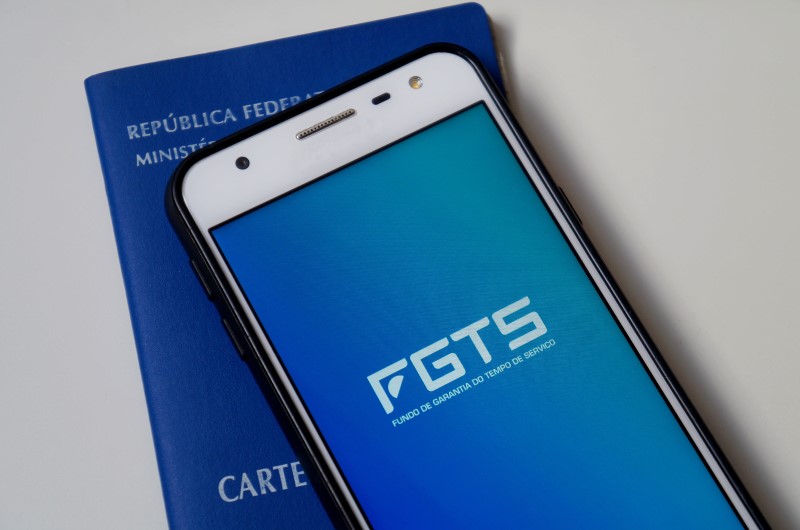 Como funciona o FGTS | Foto da Carteira de Trabalho e de um celular com o logo do FGTS | Como limpar o seu nome