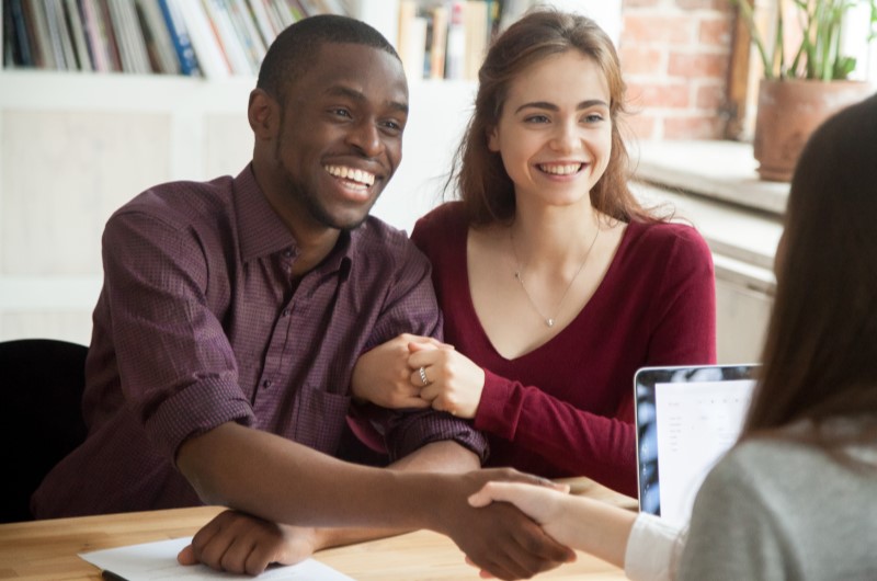  Foto de um casal feliz fechando acordo com a corretora de imóveis | Dúvidas sobre dívidas | Eu Dou Conta