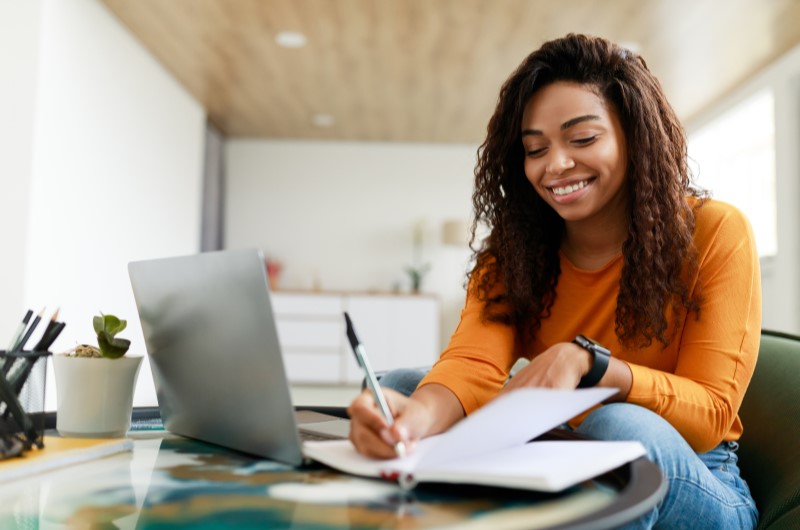 Organizando as contas | Mulher sorridente escrevendo em um caderno | Como limpar o seu nome