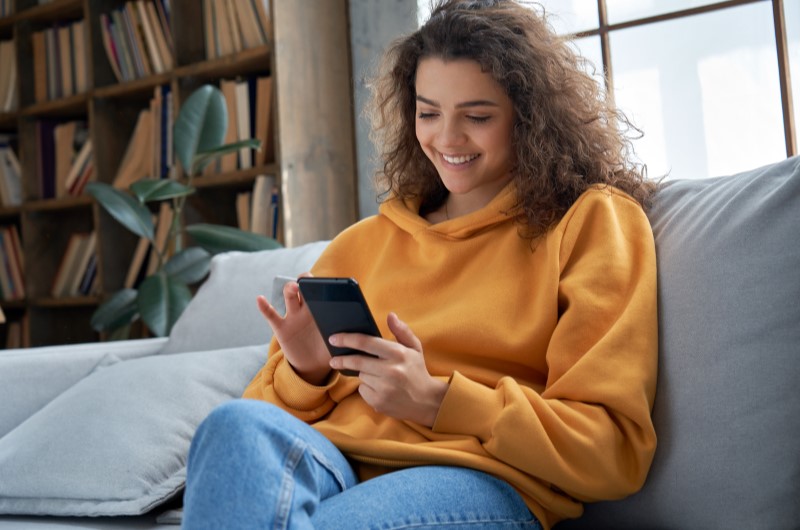 Tipos de investimento | Foto de uma Mulher olhando feliz para o celular | Economia e renda extra | Eu Dou Conta