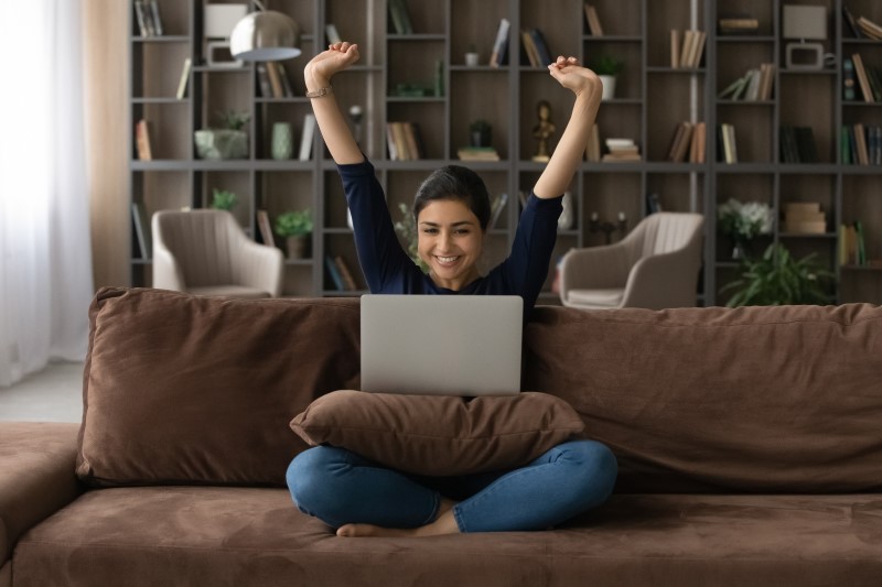 Como limpar o nome | Foto de uma mulher feliz pesquisando na internet | Dúvidas sobre dívidas | Eu Dou Conta