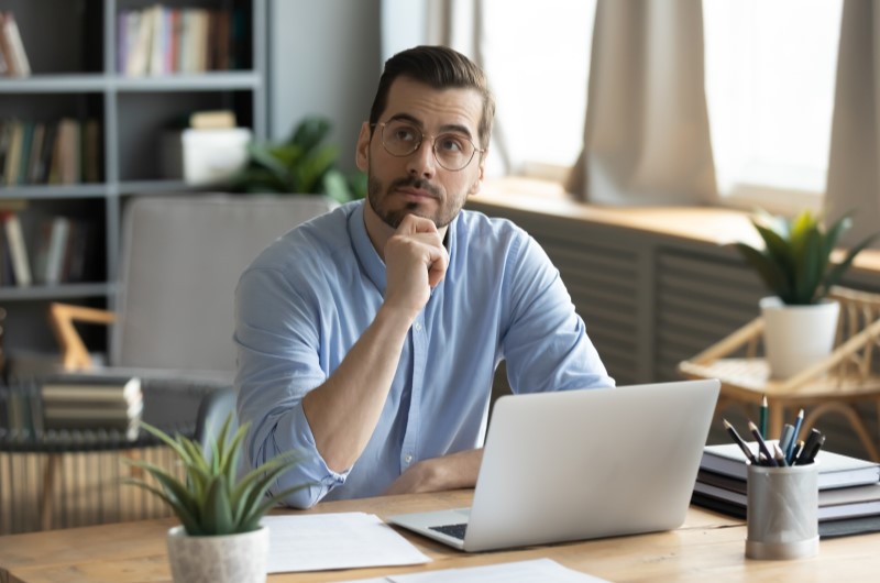 O que é o programa de afiliados | Foto de um homem pensativo mexendo no computador | Economia e renda extra | Eu Dou Conta 