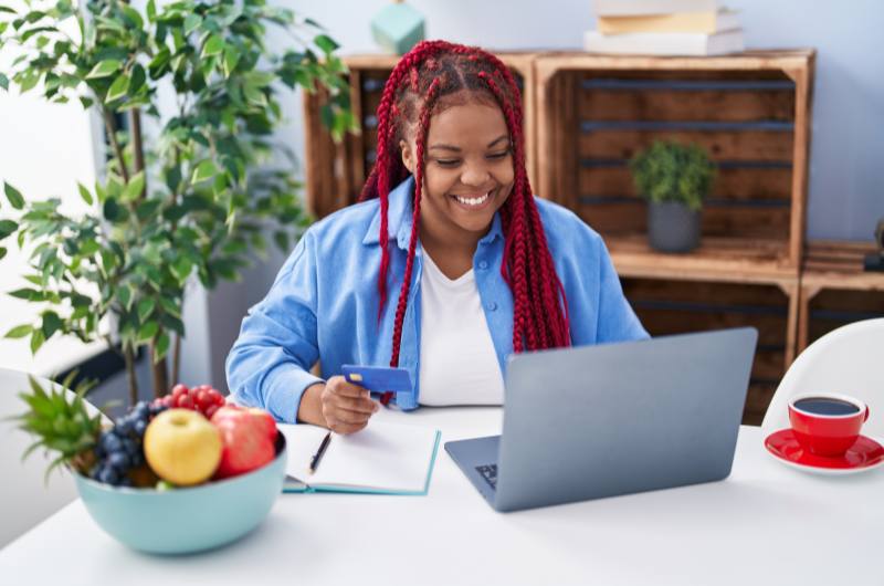 Quais as vantagens de aumentar o Score? | Foto de uma mulher sorridente pesquisando no notebook | Dúvidas sobre dívidas | Eu Dou Conta 