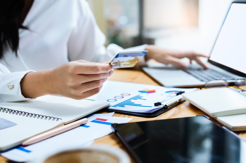 Quais bancos aderiram ao Desenrola Brasil | Foto de uma mulher com um cartão, mexendo no notebook | Como limpar o seu nome | Blog Eu Dou Conta 