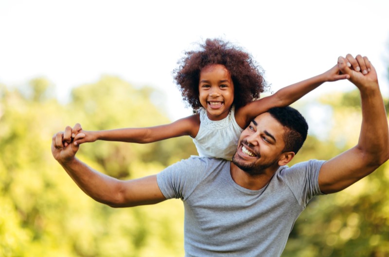 Como economizar com os presentes de Dia das Crianças | Foto de um pai brincando com sua filha ao ar livre | Economia e renda extra | Eu Dou Conta