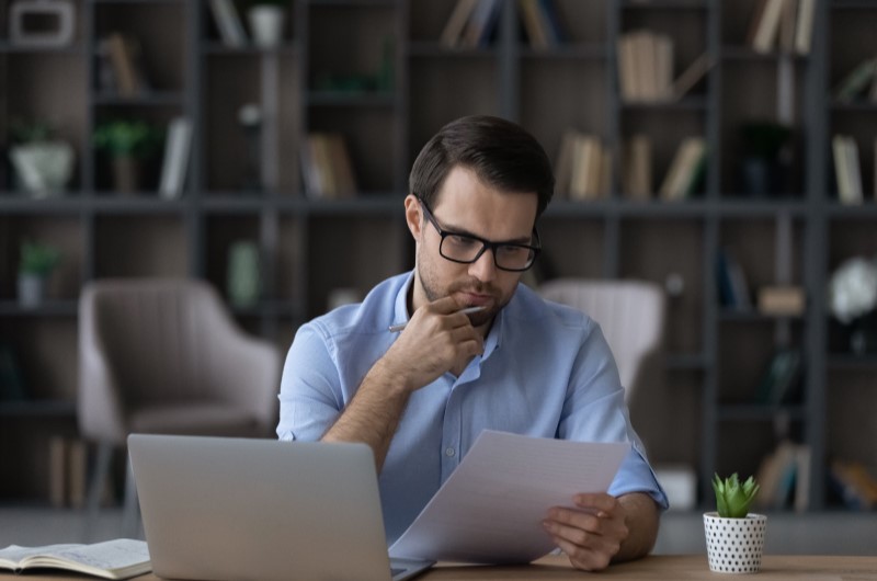 Qual a diferença entre consórcio e financiamento | Foto de um homem sério analisando um papel em frente ao notebook | Dúvidas sobre dívidas | Eu Dou Conta 