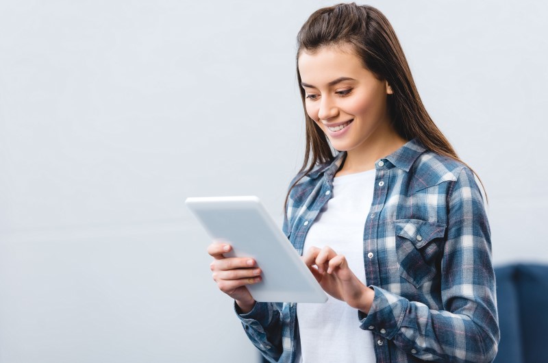 Quem pode fazer | Foto de uma mulher sorridente usando um tablet para pesquisar | Dúvidas sobre dívidas | Eu Dou Conta 