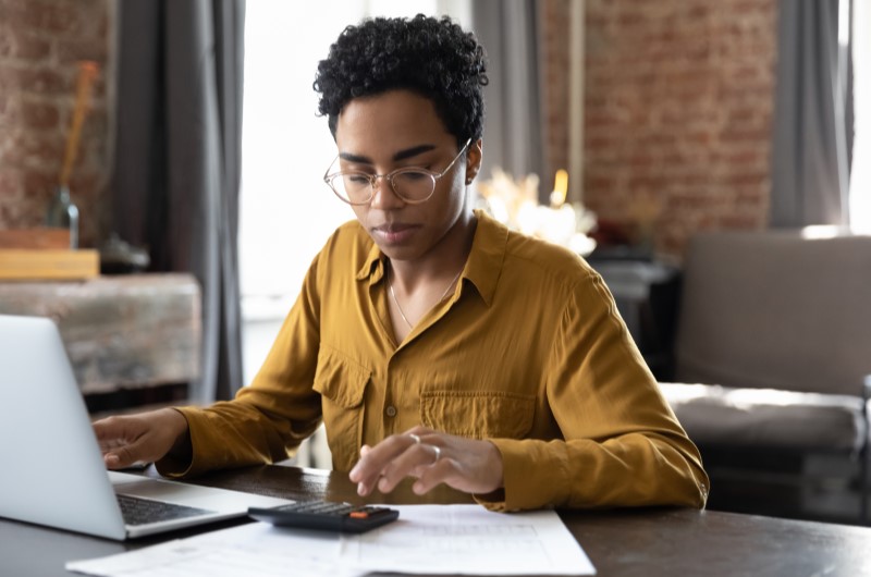 Conheça os principais tipos de investimentos para iniciantes, e entenda como começar a investir | Foto de uma mulher utilizando a calculadora com um notebook na frente | Economia e renda extra | Eu Dou Conta