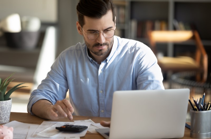 Como usar o décimo terceiro para limpar o nome? | Foto de um homem usando a calculadora e o notebook | Como limpar o seu nome | Eu Dou Conta