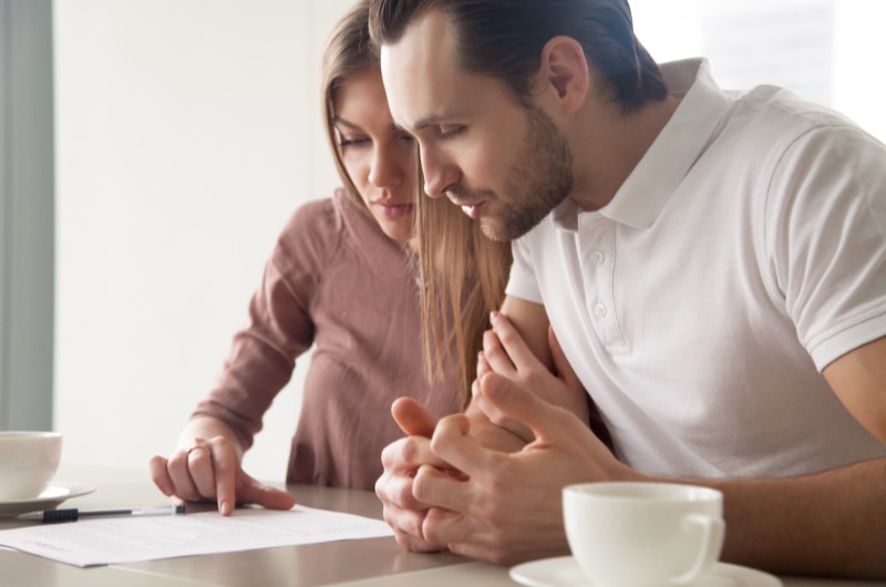 Pague a dívida de maior valor primeiro | Foto de um casal lendo um papel em cima da mesa | Como limpar o seu nome | Eu Dou Conta