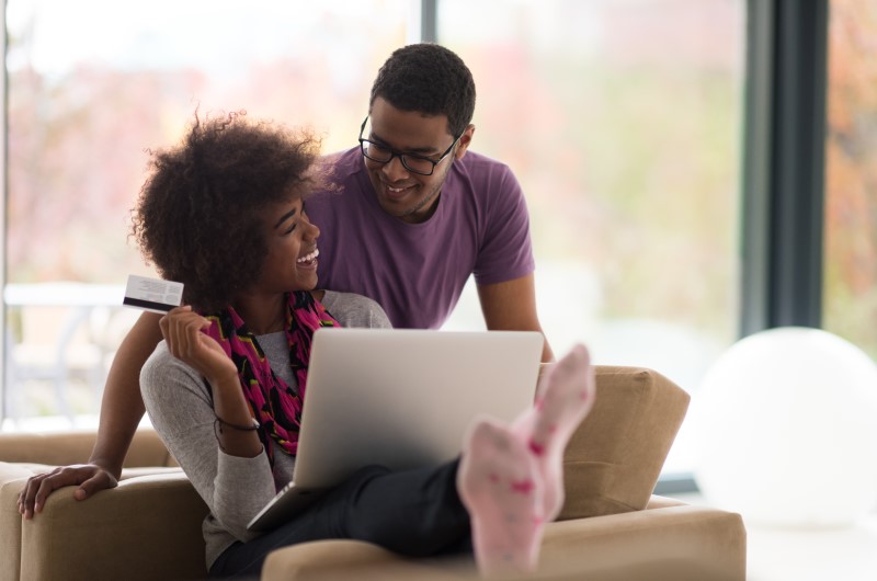 Procure cartões sem anuidade | Foto de um casal sorrindo enquanto segura um cartão e tem um notebook no colo | Economia e renda extra | Eu Dou Conta