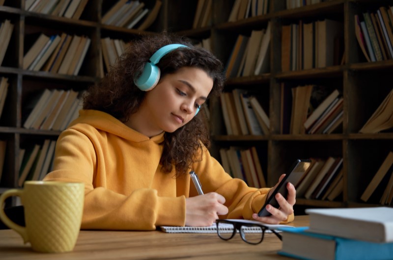 Biblioteca de São Paulo | Foto de uma moça com fone de ouvido, estudando em uma biblioteca | Trilha da Conquista | Blog da Tenda 