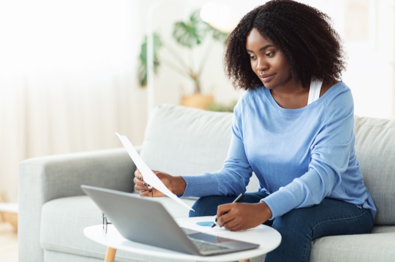 Defina um limite de gastos por categoria | Foto de uma mulher segurando um papel e usando o notebook | Economia e renda extra | Eu Dou Conta 