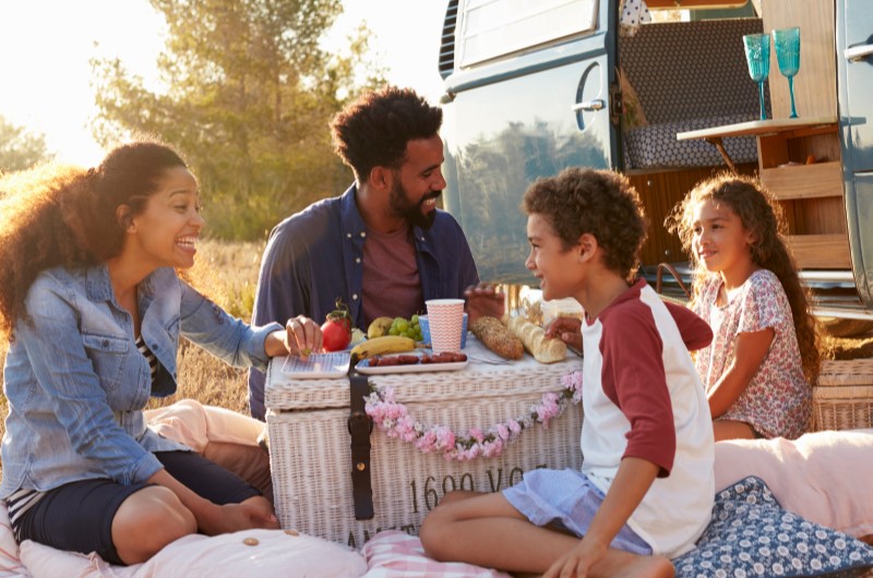 Faça um piquenique nas férias escolares | Foto de uma família feliz fazendo um piquenique ao ar livre | Economia e renda extra | Eu Dou Conta 