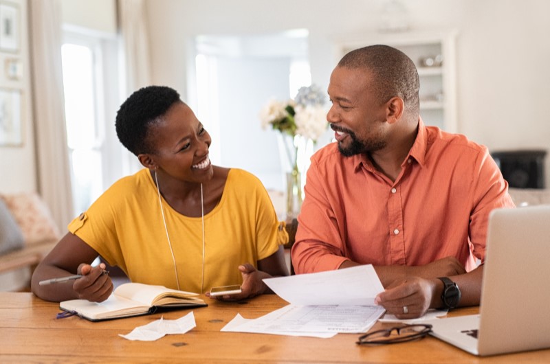 O que é educação financeira? | Foto de um casal sorrindo enquanto seguram alguns papeis | Economia e renda extra | Eu Dou Conta 