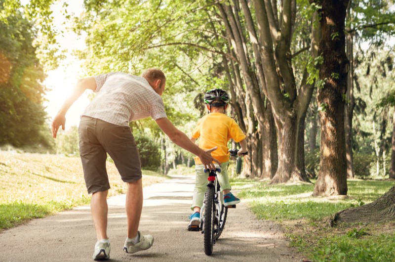 O que fazer na Zona Norte de São Paulo? | Foto de um pai ajudando seu filho a andar de bicicleta | Trilha da Conquista | Blog da Tenda 