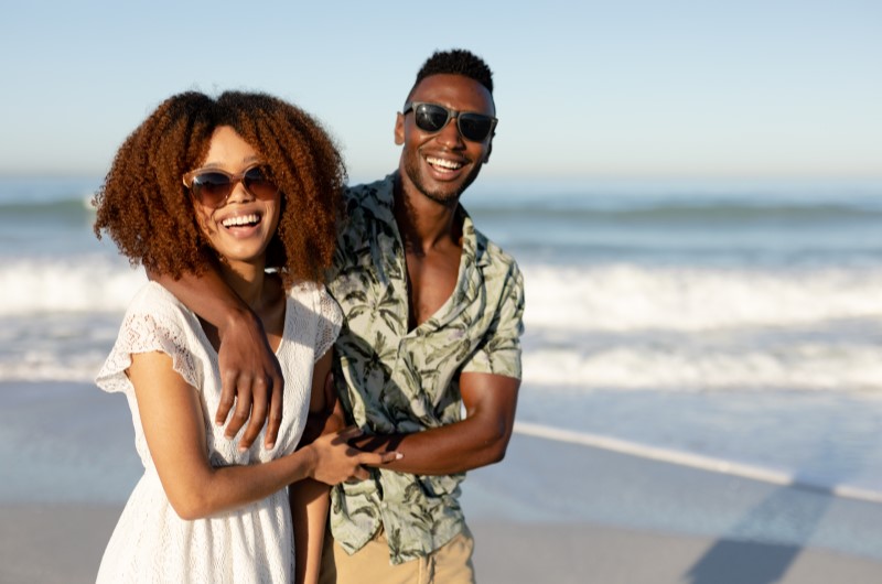 Passeios baratos: lugares para visitar no Rio de Janeiro | Foto de um casal sorridente na areia da praia | Eu Dou Conta | Blog da Tenda 