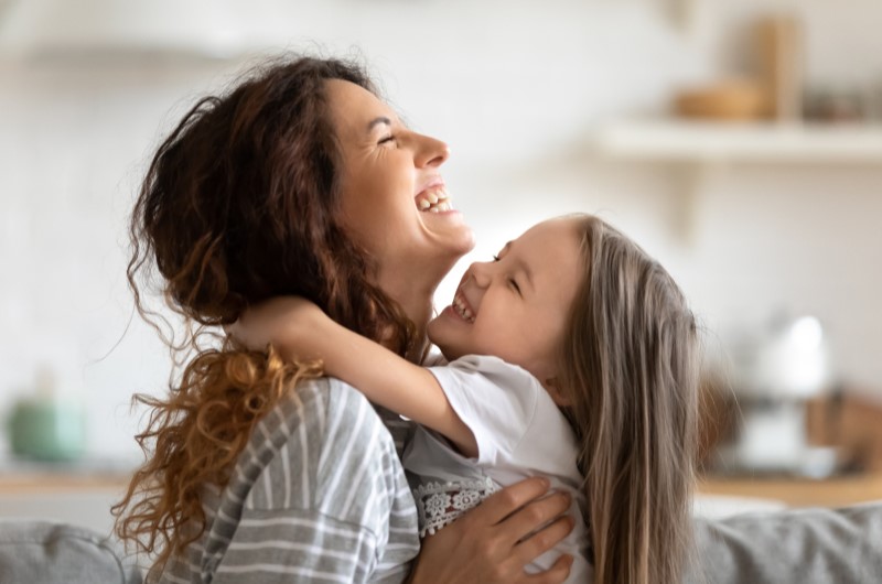 Como planejar as férias escolares? | Foto de uma mãe segurando sua filha no colo enquanto sorriem | Economia e renda extra | Eu Dou Conta 