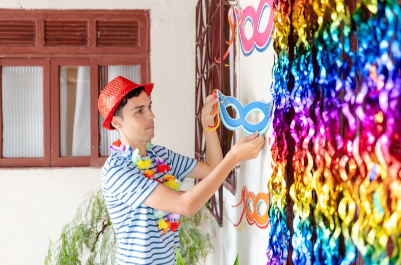 Dicas para fazer uma decoração de Carnaval criativa | Homem decorando parede com enfeites de Carnaval | Casa e Decoração | Blog da Tenda