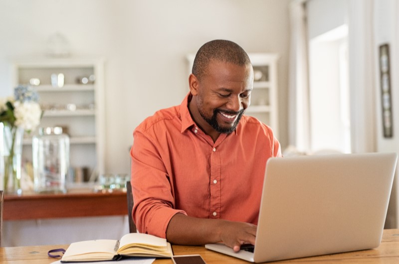 Bairros industriais | Foto de um homem sorrindo enquanto utiliza o notebook | Trilha da Conquista | Blog da Tenda