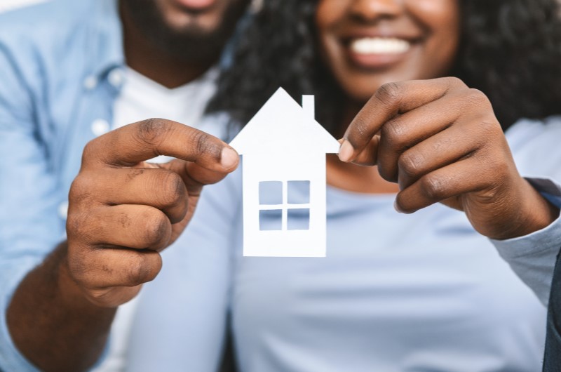 Como faço para dar entrada em um apartamento? | Foto de um casal sorridente segurando uma casinha de papel | Economia e renda extra | Eu Dou Conta 