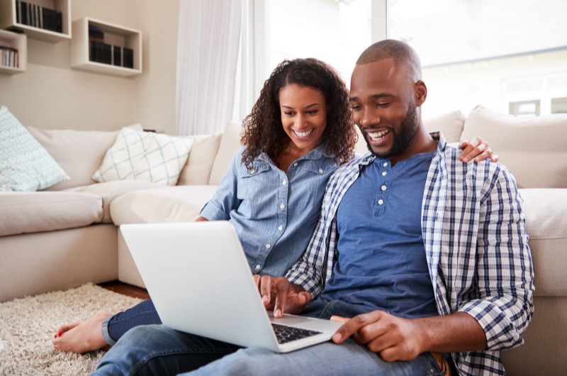 Vantagens de morar em bairros mistos? | Foto de um casal sorridente usando o notebook | Trilha da Conquista | Blog da Tenda