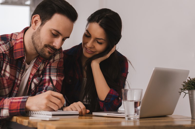 Nota Fiscal de Serviço (NFS-e) | Foto de um casal aotando em uma agenda, com um notebook sobre a mesa | Dúvidas sobre dívidas | Eu Dou Conta 