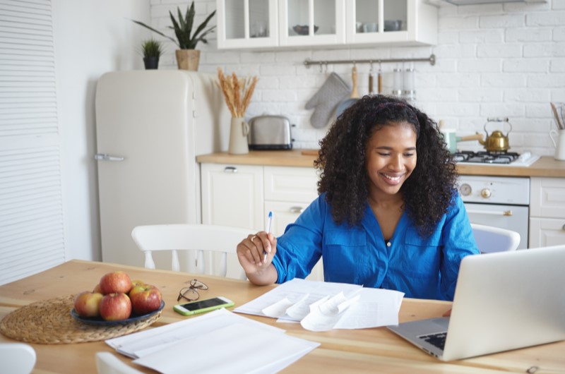 O que é Nota Fiscal? | Foto de uma moça sorridente usando o notebook, com diversos papeis na mesa | Dúvidas sobre dívidas | Eu Dou Conta 