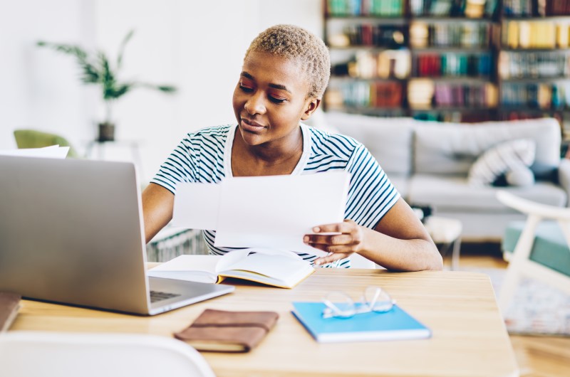 Qual a importância de organizar as finanças pessoais? | Foto de uma mulher segurando um papel na frente do notebook | Economia e renda extra | Eu Dou Conta 