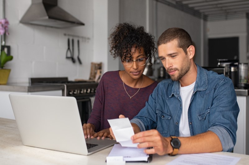 Defina um limite de gastos | Foto de um casal usando o notebook e olhando para um papel | Dúvidas sobre dívidas | Eu Dou Conta 