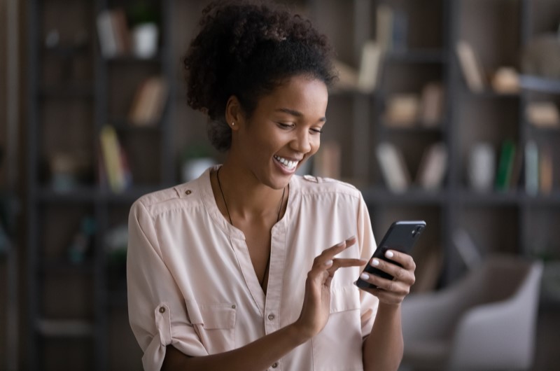 Experimente usar o débito automático | Foto de uma mulher sorridente usando o celular | Dúvidas sobre dívidas | Eu Dou Conta 