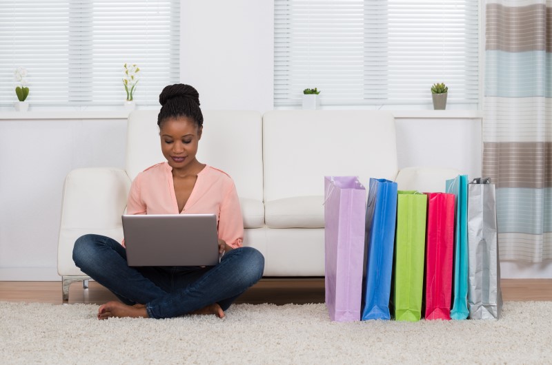 O que são compras por impulso? | Foto de uma moça usando o notebook, com sacolas de compra ao lado | Economia e renda extra | Eu Dou Conta 