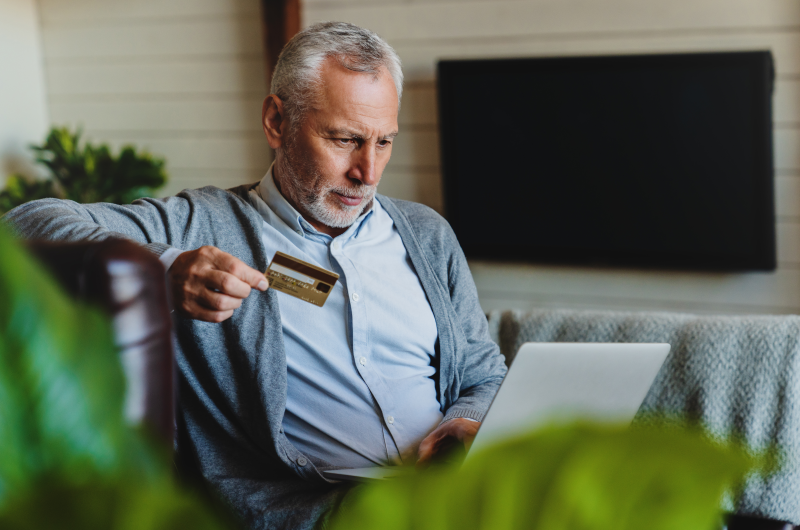 Principais causas da inadimplência | Foto de um homem usando o notebook e segurando um cartão | Dúvidas sobre dívidas | Eu Dou Conta