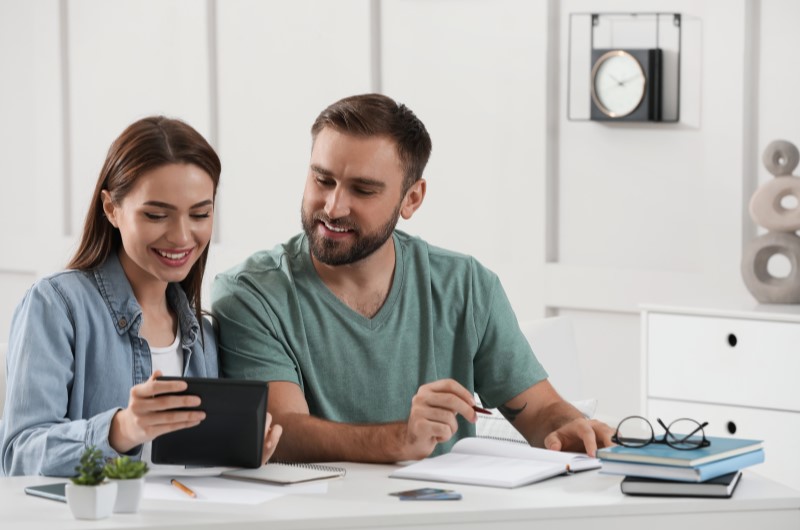 Redução dos gastos desnecessários | Foto de um casal sorridente organizando as finanças da casa | Economia e Renda Extra | Eu Dou Conta 