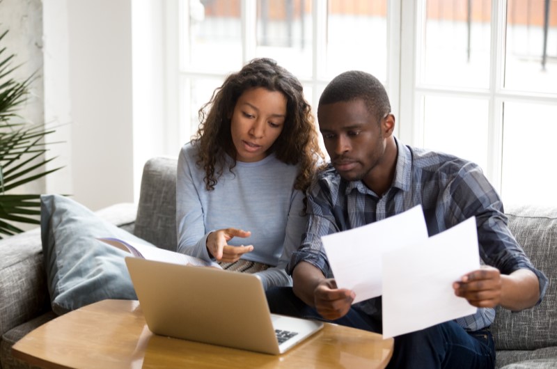 Como saber se caí na malha fina? | Foto de um casal segurando alguns papeis e olhando para o notebook | Dúvidas sobre dívidas | Eu Dou Conta 