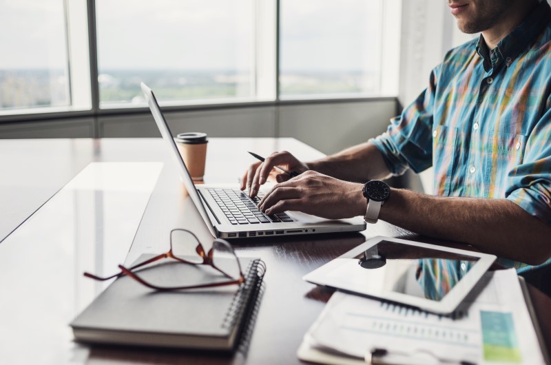 Quem precisa declarar Imposto de Renda? | Foto de um homem usando o notebook com um caderno, óculos e tablet ao lado | Dúvidas sobre dívidas | Eu Dou Conta 