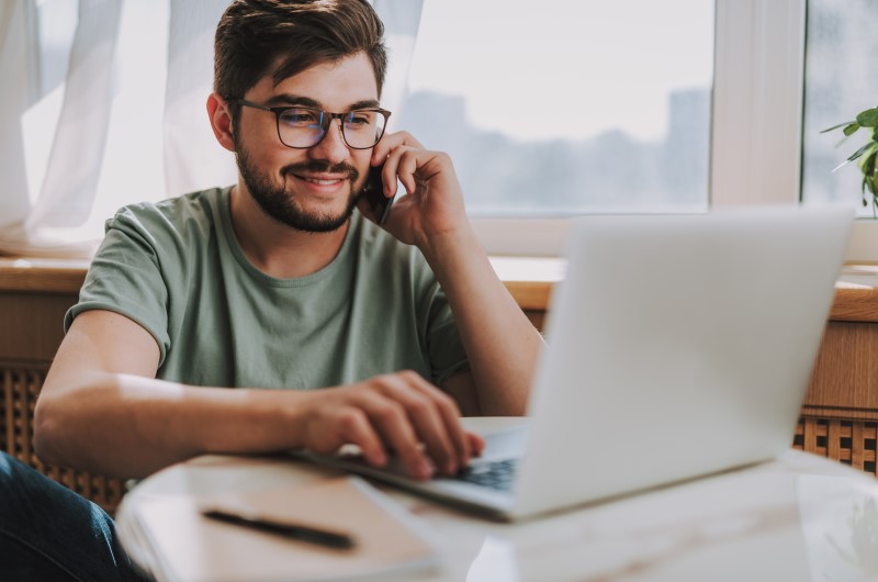  Como fazer uma indicação no Eu Indico a Tenda? | Foto de um homem usando o celular enquanto usa o notebook | Economia e Renda Extra | Eu Dou Conta 