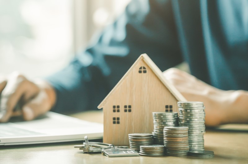 Como saber o valor do meu subsídio? | Foto de uma pessoa ao fundo, com uma casinha e moedas a frente | Minha Casa Minha Vida | Blog da Tenda