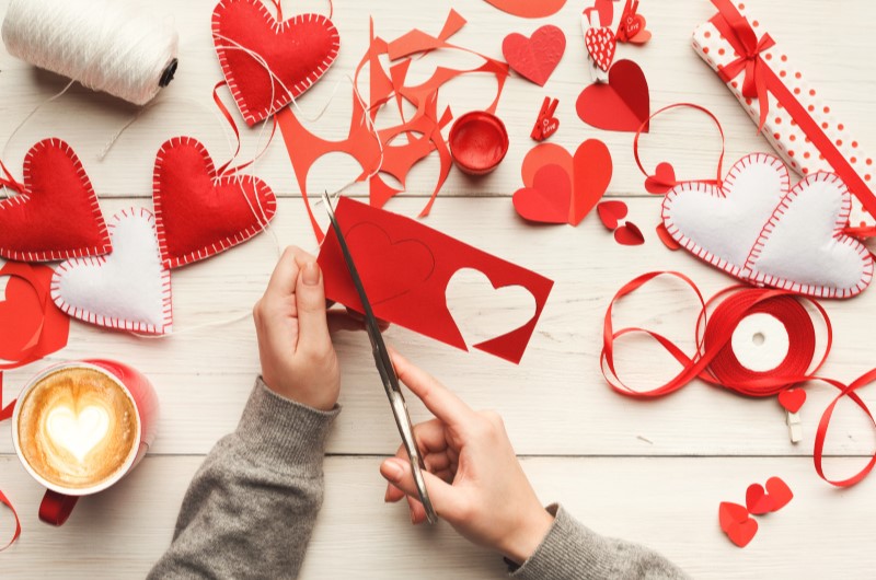 Opte por opções DIY (faça você mesmo) | Foto de uma pessoa recortando um coração de papel e diversas decorações ao redor | Blog da Tenda