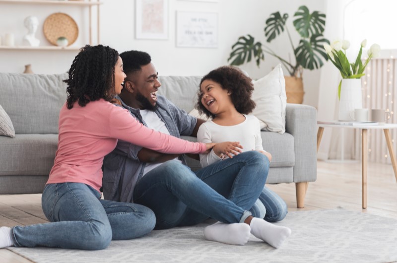 Por que as pessoas escolhem morar no bairro Taquara no Rio de Janeiro | Foto de uma família feliz se divertindo na sala de estar | Trilha da Conquista | Blog da Tenda