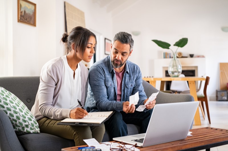 Qual a importância da organização da vida financeira | Foto de um casal na sala organizando as contas com um caderno e um noebook | Como limpar o seu nome | Eu Dou Conta 