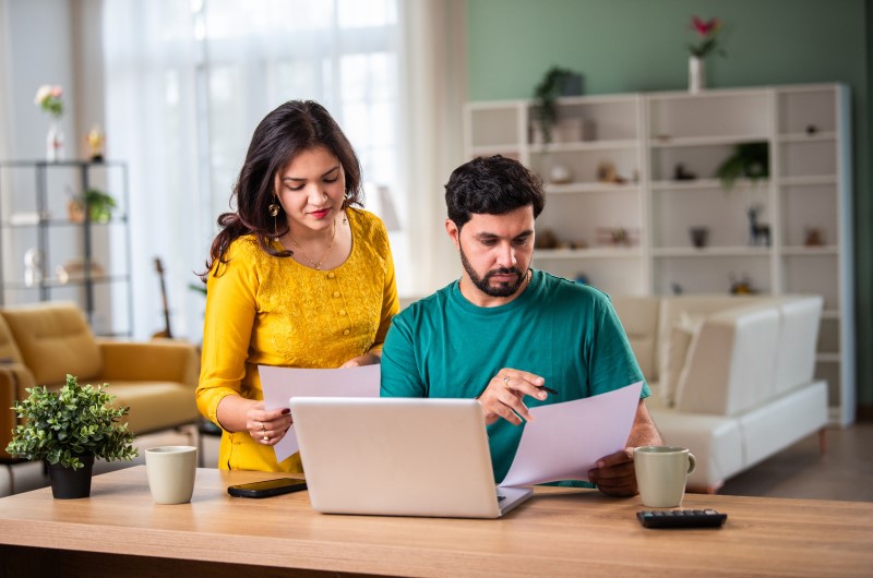 Acompanhe o seu score de crédito | Foto de um casal segurando alguns papeis na frente do notebook | Como limpar o seu nome | Eu Dou Conta 