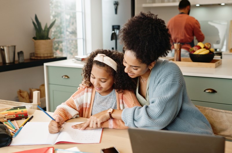 Defina limites e rotinas nas férias escolares | Foto de uma mãe e filha fazendo atividades em um caderno | Viver em condomínio | Blog da Tenda