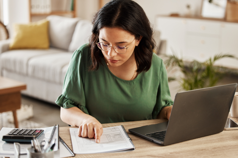 Maior preparo para imprevistos e emergências | Foto de uma mulher organizando as finanças com um caderno, um notebook e uma calculadora | Economia e renda extra | Eu Dou Conta